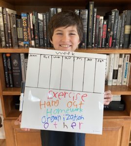 Image of boy smiling holding a white board with a weekly schedule a to do list
